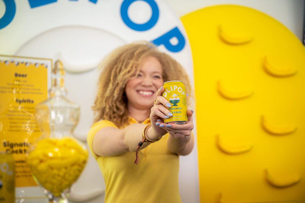 Champion holding a yellow Olipop banana cream soda beverage can in front of a Play Yellow event display.