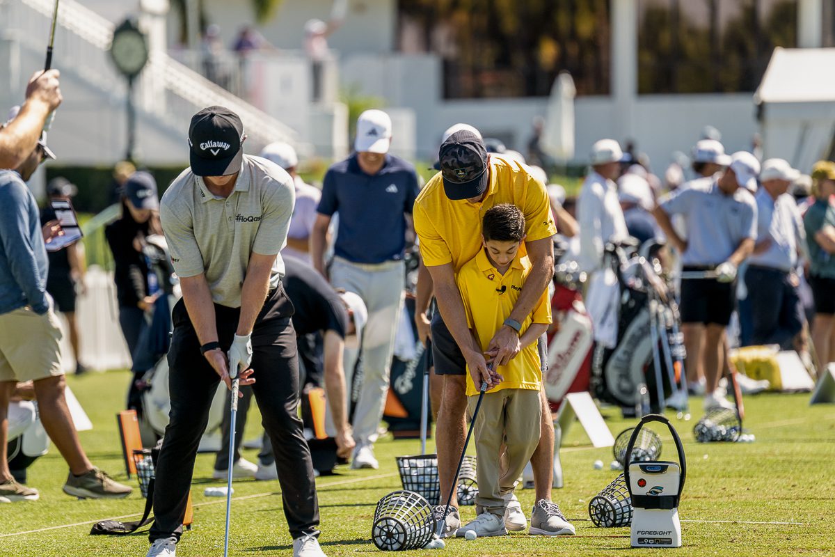 Adult helping a young Play Yellow champion line up a golf shot at a practice range.