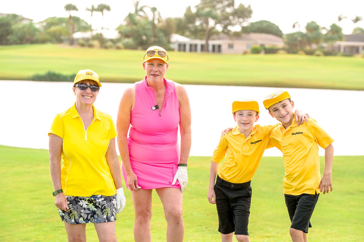 Two adults and two young golfers posing together on a golf course during a Play Yellow event.