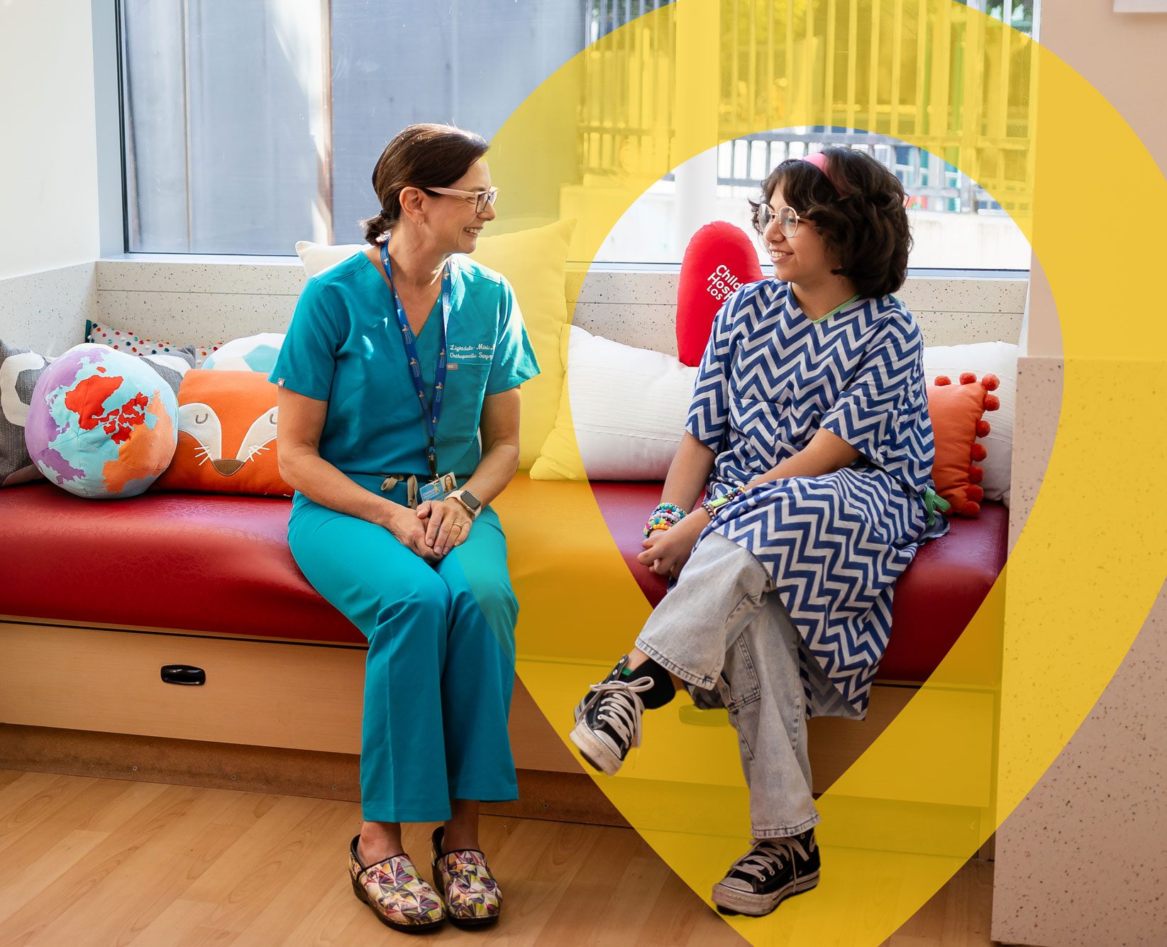 Child sitting with a hospital staff member in a children’s hospital room.