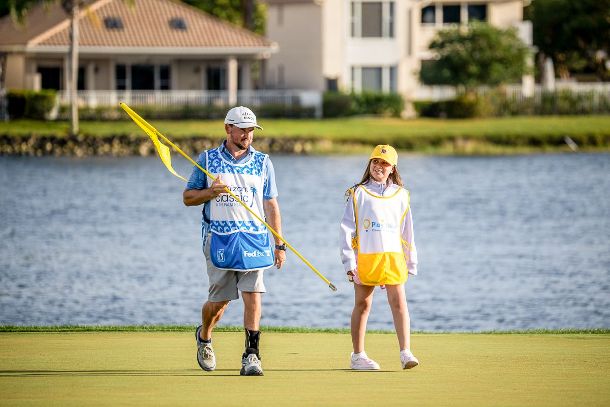 Young Play Yellow participant walking on a golf course with a tournament caddie.