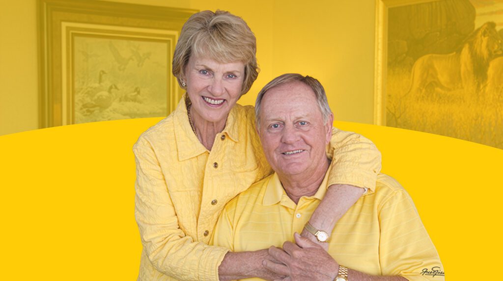 A studio portrait of Barbara and Jack Nicklaus smiling together; Barbara is wearing a textured yellow jacket and Jack is in a yellow polo shirt, set against a yellow background with framed nature artwork.